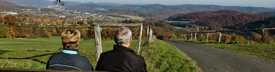 Paar auf einer Bank mit Blick über die herbstliche Mittelgebirgslandschaft im Lahn-Dill-Kreis nahe dem Ferienhaus Scheldequelle in Eschenburg